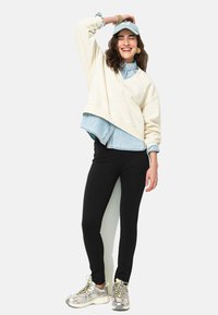 Sweatshirt crème, chemise en denim bleue en dessous, leggings noirs et baskets argentées. Le sweatshirt a une coupe décontractée et un design en V.
