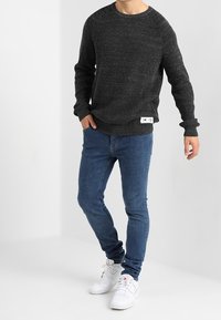 Mörkgrå ribbad tröja med rund halsringning, kombinerad med slim-fit blåjeans och vita sneakers. Märkbar varumärkesskylt på tröjan.