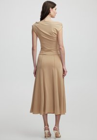 Beige jurk met een aansluitende lijfje en een vloeiende rok. Zacht, rekbaar materiaal en geplooide schouderdetails. Lengte tot halverwege de kuiten, gecombineerd met lichte hakken.