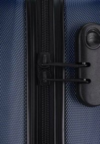 Blue textured suitcase corner featuring a black zipper and dual zipper pulls, with a black lock mechanism for added security.