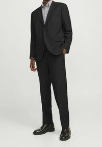 Czarny garnitur z marynarką na jeden guzik, klapami w kształcie notcha, dwoma przednimi kieszeniami, w połączeniu z czarnymi eleganckimi butami i w paski koszulą pod spód.