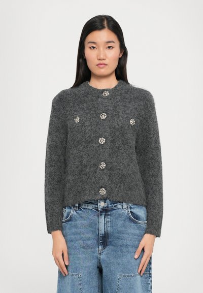 Gilet en tricot gris avec un col rond, orné de cinq boutons floraux, et un ourlet côtelé, associé à un jeans bleu clair.