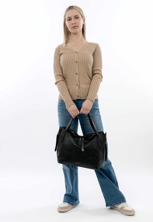 Schwarze Handtasche mit strukturiertem Design, glatter Lederoberfläche, doppelten Tragegriffen und einem Reißverschlussakzent. Trägt eine Person in einem beigen Oberteil und Jeans.