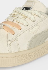 Κοντινή λήψη μπεζ αθλητικού παπουτσιού Puma Suede με υφασμάτινη σόλα, χοντρές πλεκτές κορδόνια και λεπτομέρειες από μπεζ δέρμα και ύφασμα.