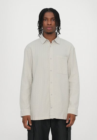Chemise boutonnée gris clair avec texture verticale, poche poitrine et manches longues. Fabriquée en tissu doux, elle présente un col classique et des boutons.