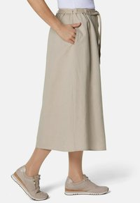 Beige, knielanger Rock mit einem Gürtel in der Taille und Seitentaschen, kombiniert mit hellbeigen Sneakers mit texturierter Oberfläche und weißen Sohlen.