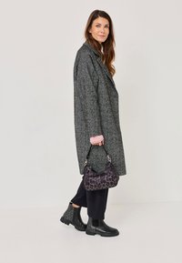 Abrigo largo gris texturizado, acentuado con mangas rosas, pantalones amplios negros y botines negros brillantes, acompañados de un bolso de mano con estampado de leopardo.