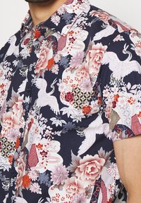 Korte mouwen overhemd met een marineblauwe achtergrond en ingewikkelde bloemen- en kraanvogelpatronen in roze, wit en roodtinten; knoopsluiting.