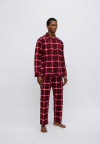 Σετ πιτζάμες από καρό φανέλα σε κόκκινο και μαύρο με κουμπιά, μακριά μανίκια και παντελόνι που ταιριάζει. Μαλακή υφή με άνετη εφαρμογή.