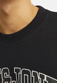 Sort bomulds sweatshirt med ribbet crew neck, prydet med fed hvid skrift på forsiden og en glat tekstur.