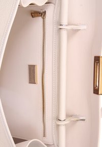 Witte leren handtas interieur met een ritsvak, metalen hardware en een label dat aangeeft dat het echt leer is. Gladde textuur, minimalistisch ontwerp.