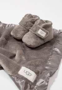 Grijze pluche babyschoentjes met een klittenbandsluiting en een zachte afwerking, gecombineerd met een bijpassende grijze pluche deken met satijnen rand en een logo-label.