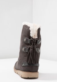 Botte en suède grise avec doublure en fausse fourrure, ornée d'accents en cuir et de pampilles, dotée d'une semelle plate en caoutchouc et de détails à bouton-pression.