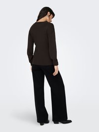 Langärmliges, dunkelbraunes Oberteil mit lockerem Sitz, Rundhalsausschnitt und angesetzten Schulternähten, kombiniert mit hoch taillierter, schwarzer, weit geschnittener Hose.