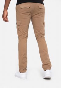 Beige cargobroek met een smalle pasvorm, voorzien van meerdere zijzakken en een gladde textuur. Gecombineerd met witte sneakers voor contrast.