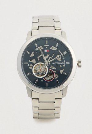Silver automatic wristwatch with skeleton dial, visible gears, black face, silver hour markers, and metal link bracelet.