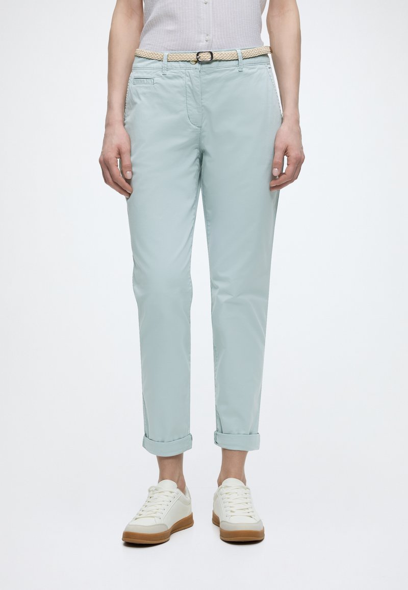 Άτομο που φοράει ανοιχτό μπλε chinos με γυρισμένα μπατζάκια, μπεζ πλεκτή ζώνη, λευκά αθλητικά παπούτσια με καφέ σόλες και λευκή αμάνικη μπλούζα.