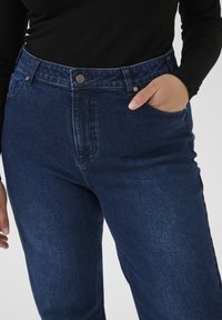 Mørkeblå denimjeans med høj talje, to forlommer og metalknapper i linningen. Glat tekstur med let stræk.