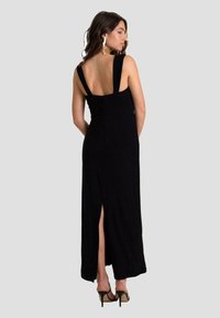 Zwarte maxi-jurk met brede bandjes, rechte rug en een zijsplit. Gemaakt van zachte stof, heeft een minimalistisch ontwerp en is gecombineerd met hoge hakken.