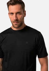 Černé sportovní tričko s krátkým rukávem vyrobené z hladkého, vlhkost-odpudivého materiálu, s diskrétním logem na hrudi, nabízející těsný střih.