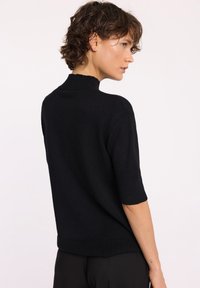 Czarny sweter dzianinowy z półgolfem, krótkimi rękawami i prążkowanym wykończeniem. Gładka faktura, dopasowany krój i minimalistyczny styl.