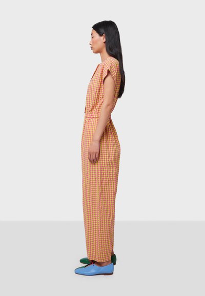 Vestido de cuadros en rosa y amarillo, con mangas cortas y cintura ceñida, combinado con zapatos planos multicolores.