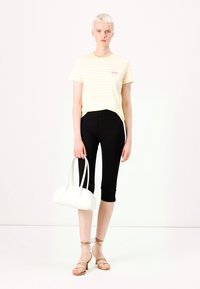 Gul och vit randig t-shirt med en liten grafik, svarta leggings och strapiga beige sandaler, kombinerat med en vit handväska.