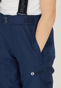 Marineblauwe sneeuwbroek met een gladde textuur, voorzien van verstelbare bandjes, een klittenbandsluiting en een zijzak met een logodetail.