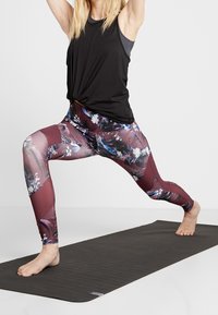 Svart linne med knuten fram, matchat med tajta leggings med maroon bas och tropiskt blommönster. Matta under.