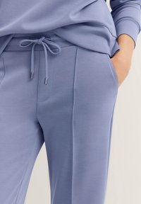 Light blue jogger pants with a smooth texture, drawstring waist, and silver tips. Features side pockets and a tailored design.