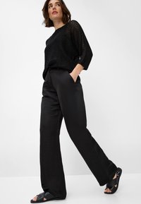 Haut en tricot noir transparent avec une coupe oversize, associé à un pantalon noir à jambes larges et des sandales plates noires. Design simple sans motifs.