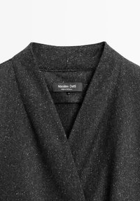 Col de manteau en laine gris foncé moucheté avec une étiquette Massimo Dutti cousue à l'intérieur, fabriqué au Portugal, présenté sur un fond clair.