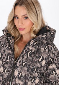 Jachetă puffer cu un model imprimat cu șarpe, având închidere cu fermoar, glugă și o combinație de culori alb-negru și bej. Material texturat cu un finisaj lucios.