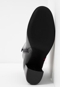 Botte à talon en cuir noir avec un bout arrondi, une fermeture éclair latérale et une semelle texturée. Présente un petit accent de couleur près du talon.