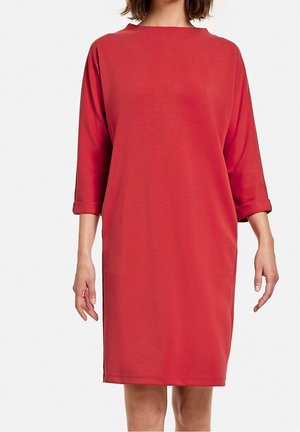 Robe rouge mi-longue en tissu doux, présentant un col bateau, des manches 3/4 et des poignets retroussés pour une coupe décontractée.