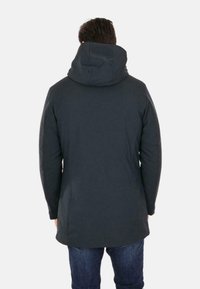 Cappotto scuro, isolato, con cappuccio, texture liscia, cuciture inclinate e orlo posteriore leggermente più lungo. Indossato sopra jeans blu.