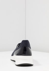 Marinblå sneaker med en strukturerad ovandel, klackkappa i lackläder och vit mellansula. Har en rund tå och en minimalistisk design.