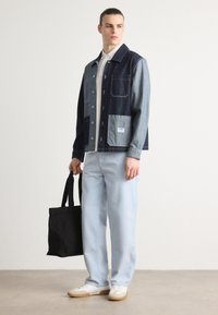 Jeansjakke med en blanding av mørke og lyse nyanser, knapplukking, to frontlommer; kombinert med lyseblå bukser og en svart totebag.