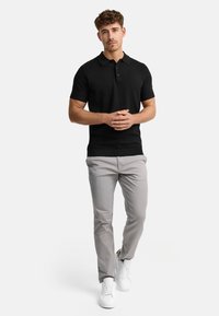 Black short-sleeve polo shirt with a ribbed texture, two-button placket, paired with light gray slim-fit trousers and white sneakers.