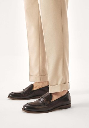 Pruunidest nahast loafers-stiilis kingad dekoratiivse rihmaga, kombineeritud helebeežide kitsenevate pükstega, millel on ülespööratud äärised. Minimalistlik disain.