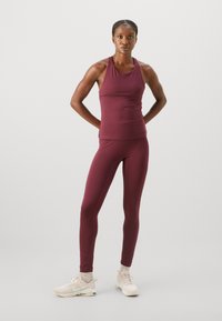 Burgundy sporttop med racerback-design som matchas med åtsittande leggings, bärs med ljusa träningsskor.