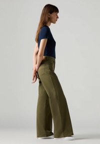 Pantalones de pierna ancha en color verde oliva con una cintura alta, elaborados con un tejido resistente. Combina con una camiseta ajustada de manga corta en color azul marino.