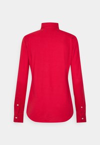 Camicia rossa a maniche lunghe con polsini abbottonati, vista da dietro su uno sfondo bianco uniforme.