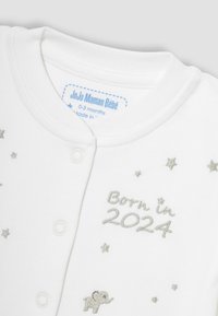 Biely bavlnený detský overal s patentkami, s striebornou výšivkou "Narodený v 2024", slonom a roztrúsenými hviezdami.