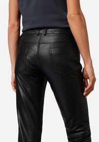 Zwarte leren broek met een aansluitend ontwerp, voorzien van achterzakken met gegolfde stiksels en een gladde textuur. Tailored tailleband inbegrepen.