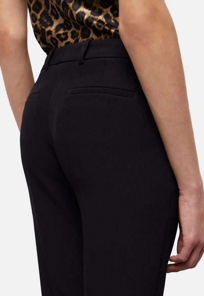 Zwarte op maat gemaakte broek met een gladde textuur, voorzien van twee achterzakken en een tailleband. De stof lijkt gestructureerd en goed aansluitend.