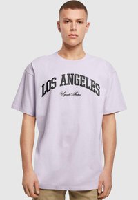 Lyslilla oversized T-shirt med "LOS ANGELES" i fed sort skrifttype og en mindre skrifttype nedenfor. Korte ærmer, crew neck design.