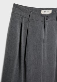 Graue plissierte Hose aus strukturiertem Stoff, mit Knopfverschluss und einem Etikett mit Größenangabe.