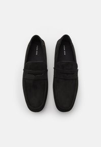 Černé semišové slip-on boty s hladkým povrchem, oválným špičkou a nenápadnými detaily v prošívání. Název značky je viditelný na vnitřní straně.