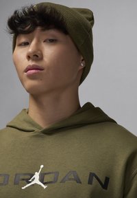 Felpa con cappuccio verde oliva con lettering nero "JORDAN" e logo Jumpman bianco; indossata con un berretto a coste abbinato; tessuto di trama liscia.